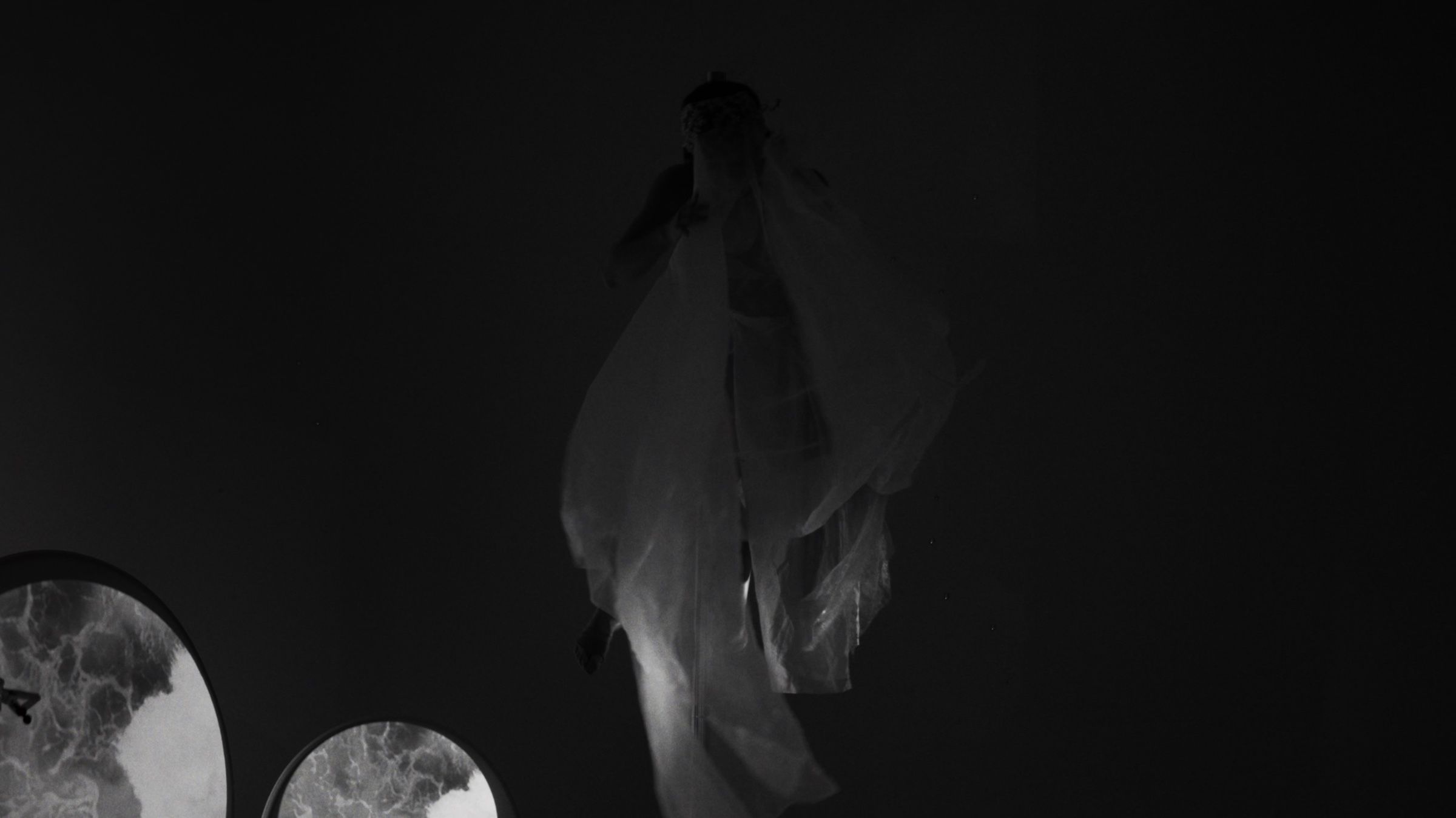 Black and white: a dancer in flowing white fabric turns in darkness.