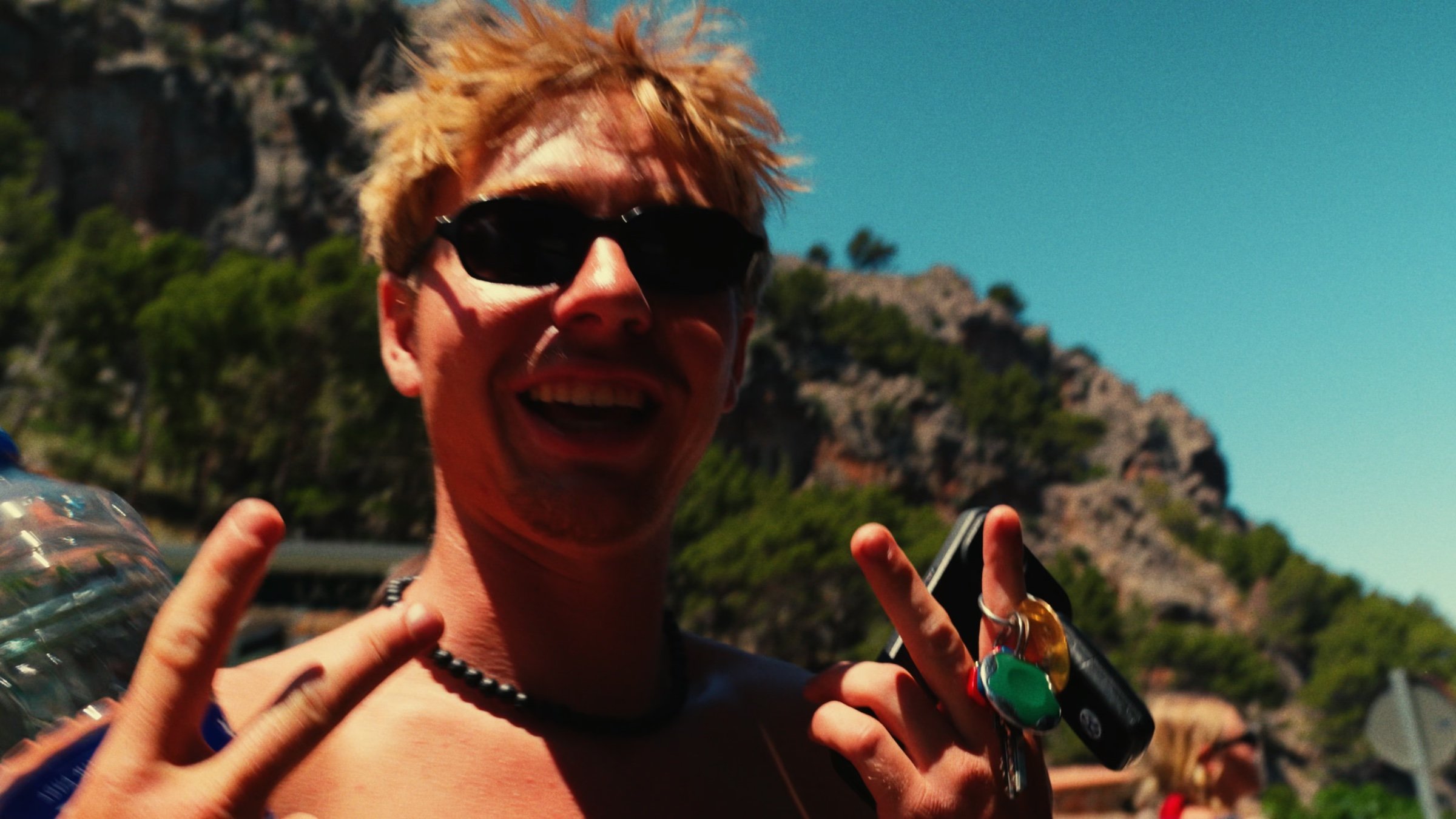 A grinning friend in sunglasses flashes a peace sign against the mountains.