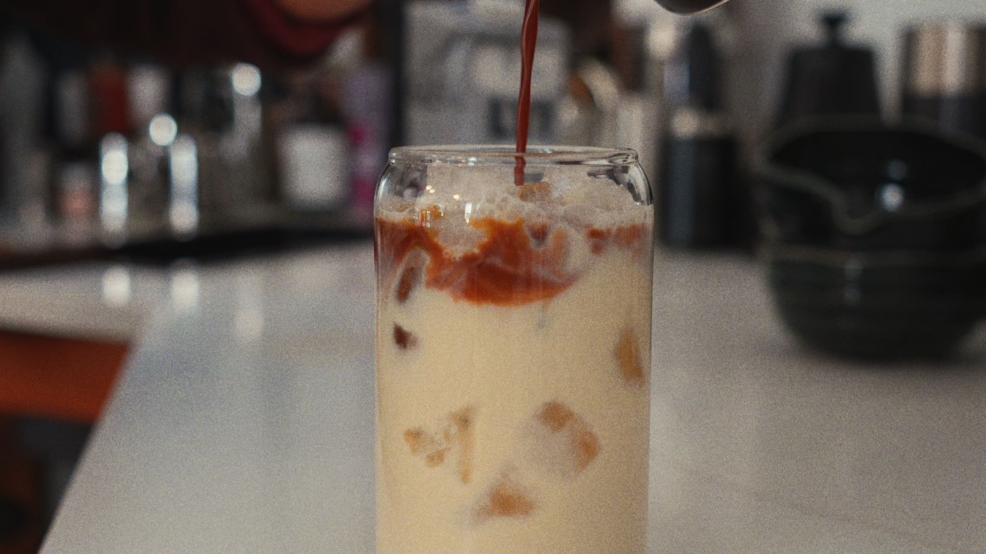 Coffee pours over ice in a tall glass.