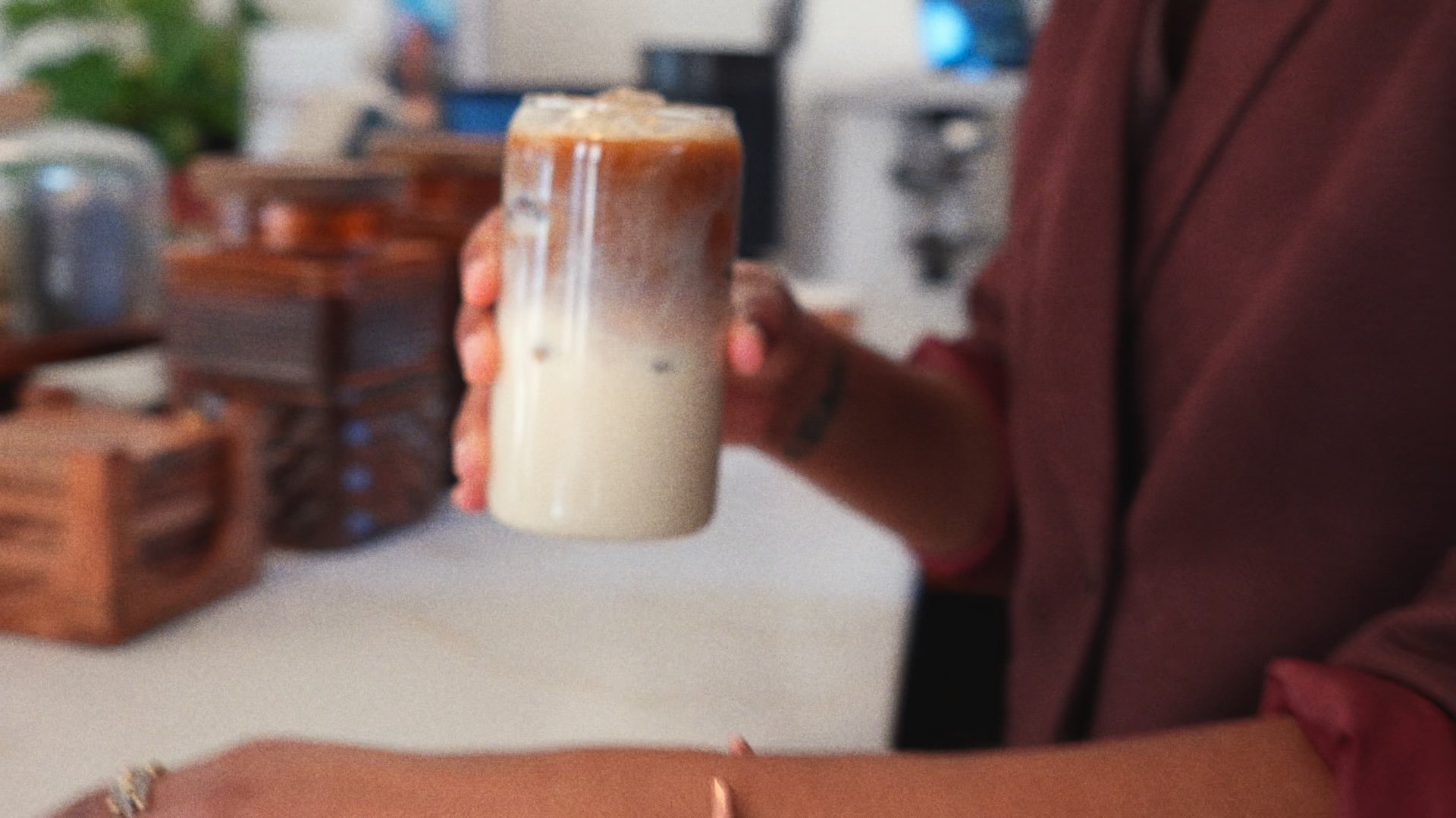 A hand lifts an iced latte from the counter.