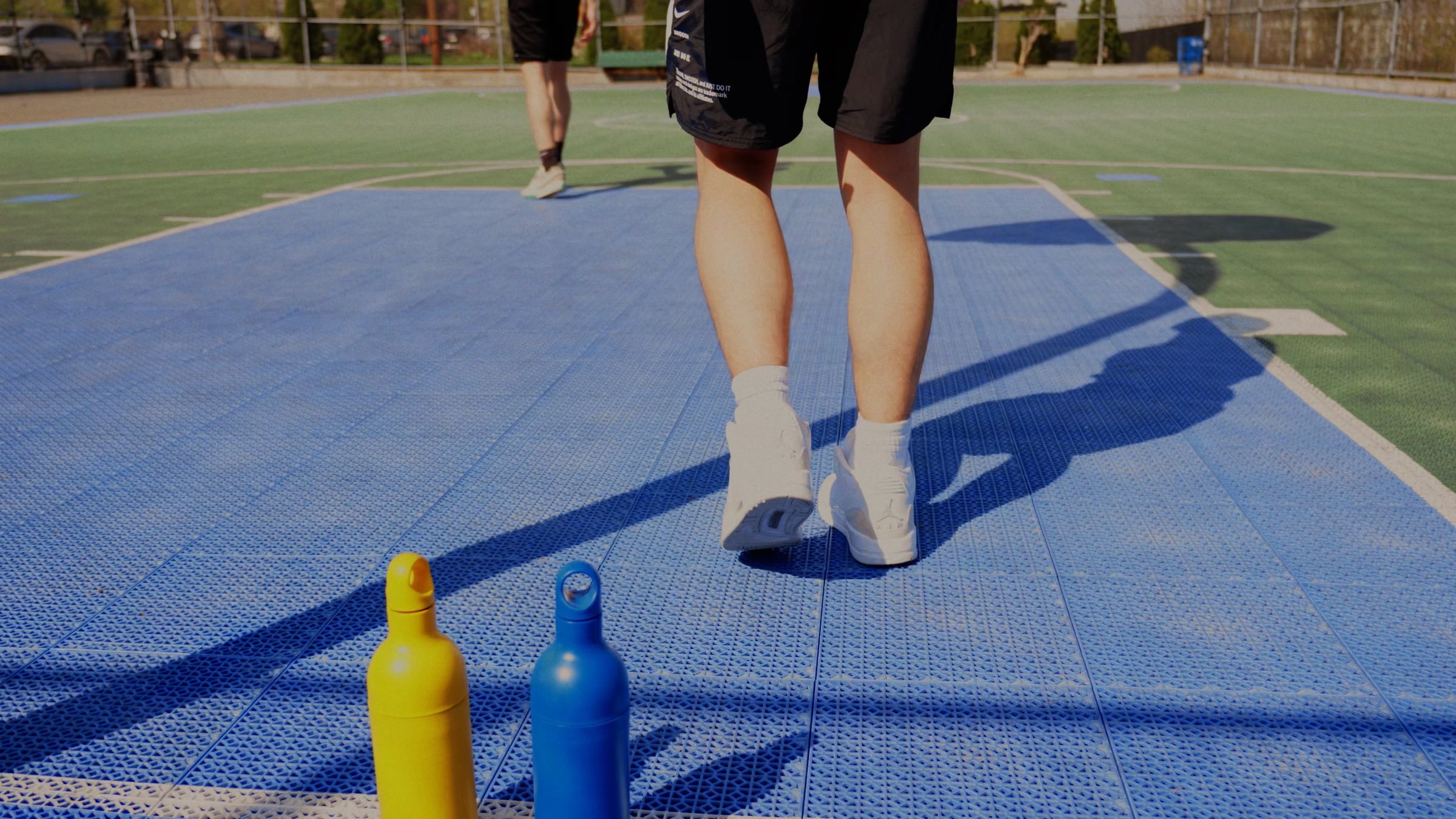 Low angle of sneakers walking across a blue court toward two bottles.