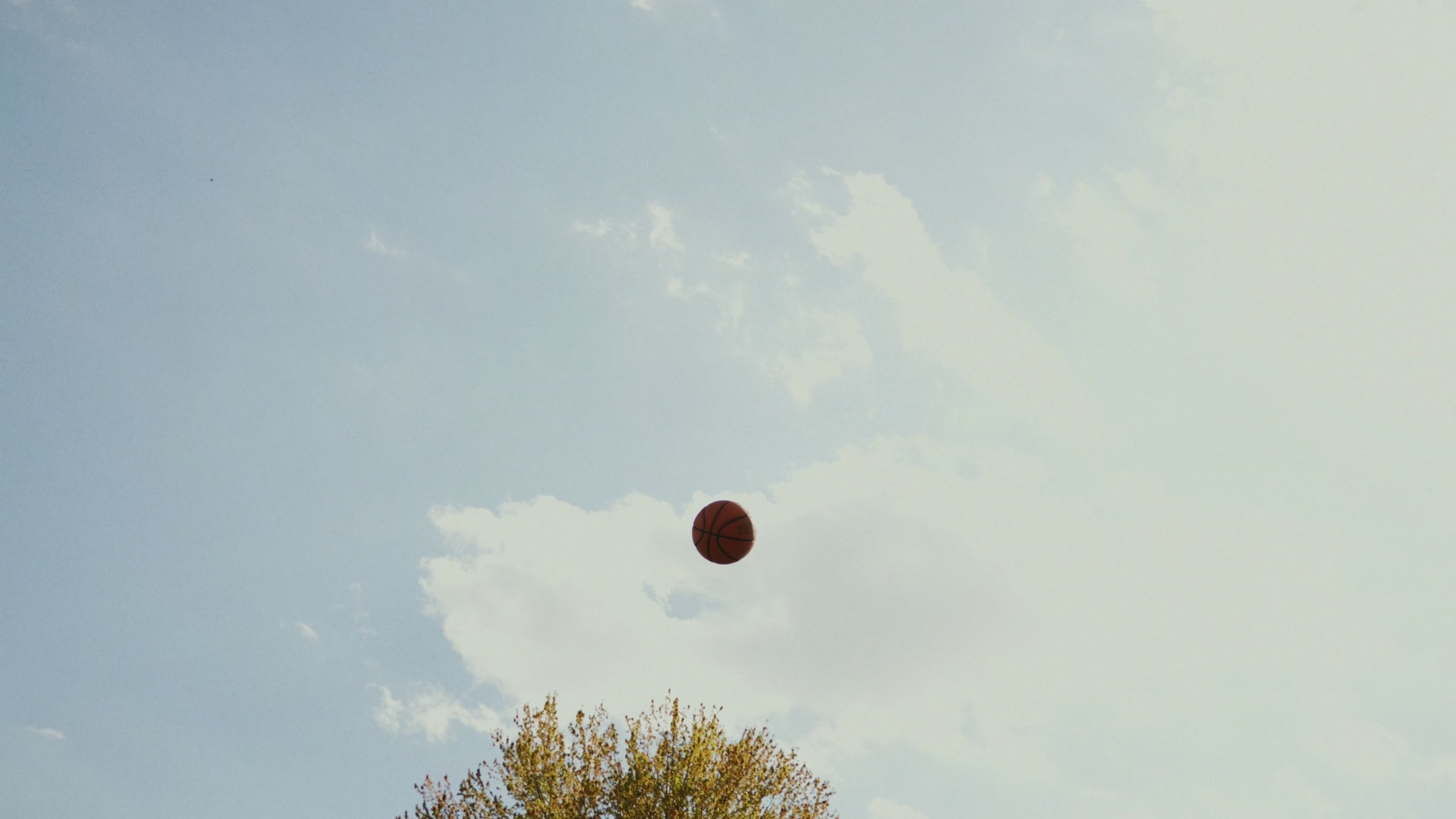 A basketball hangs in an open blue sky.