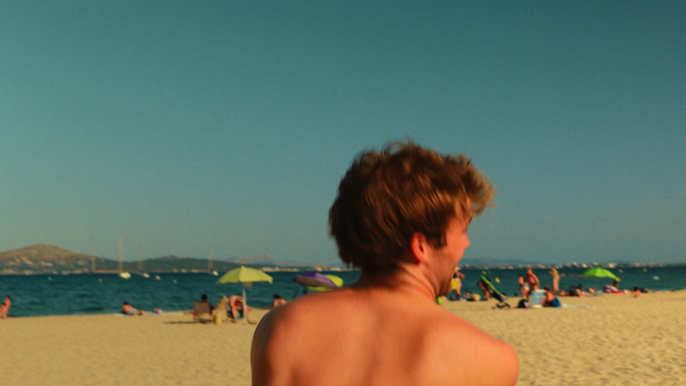 A man seen from behind, looking out over a crowded beach.