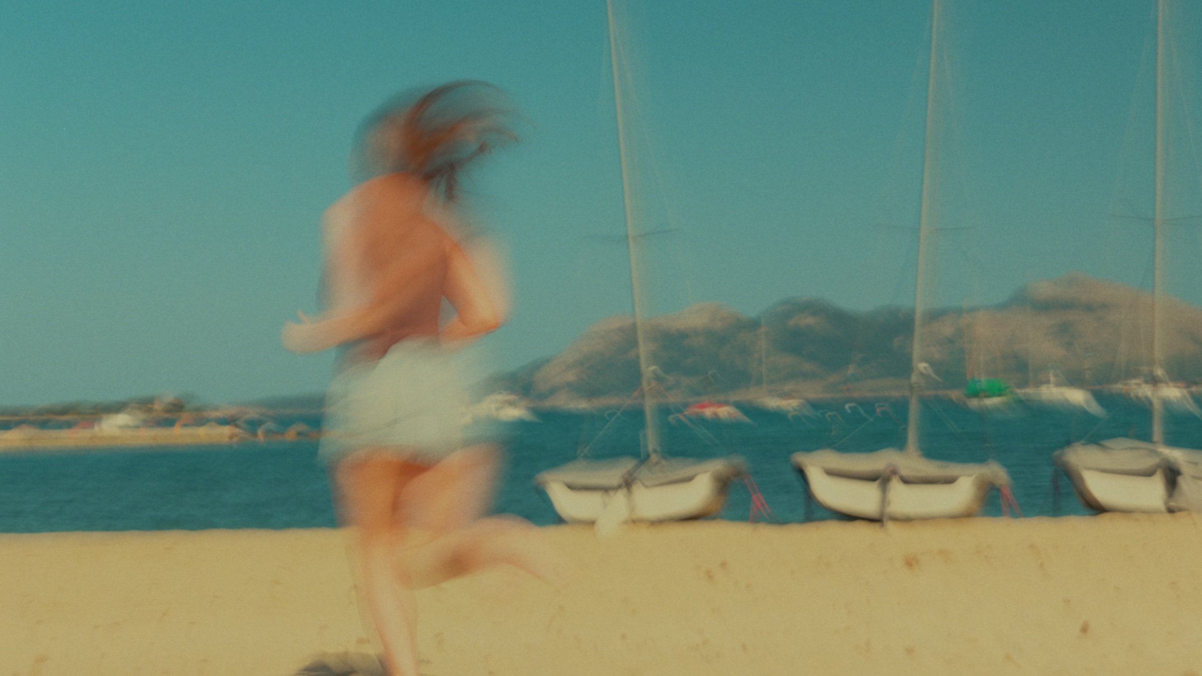 A woman runs along the shoreline past moored sailboats.