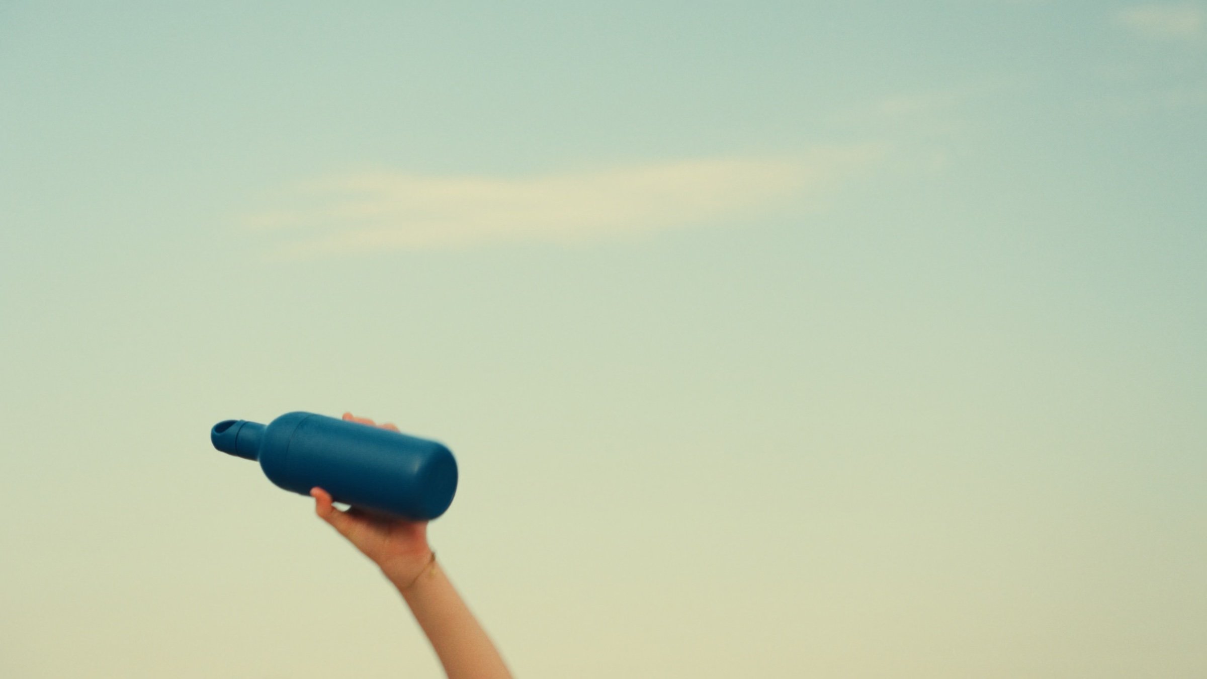 A hand holds a blue bottle up against the sky.