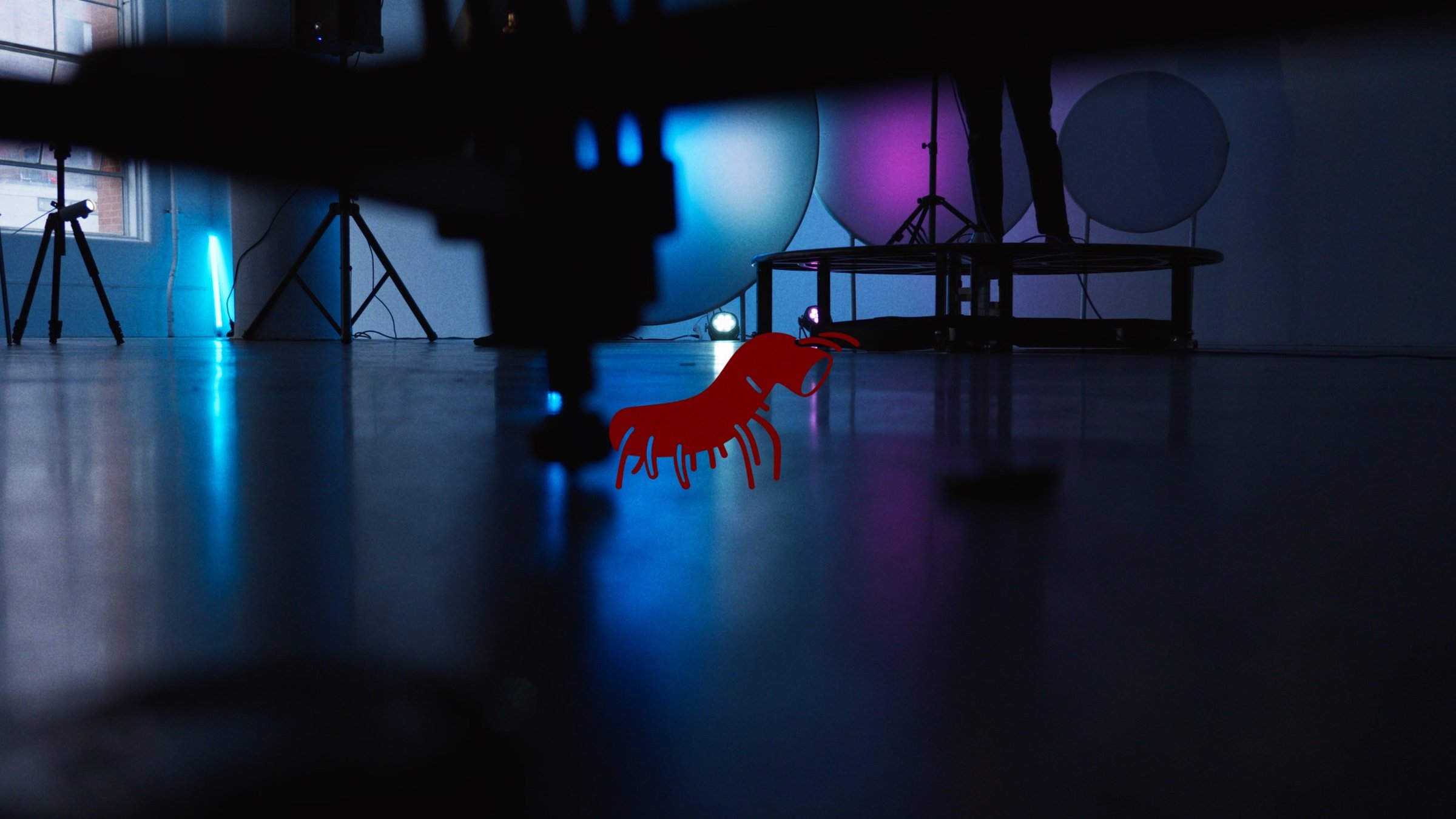 The red NYMPH creature mark on the floor of a dark studio lit in blue and violet.