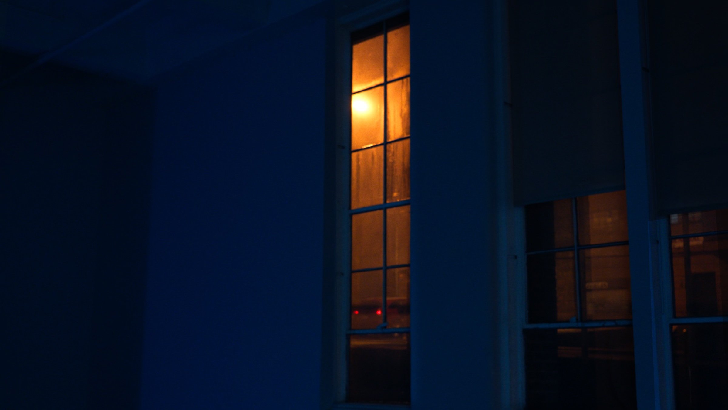 A single warm window glows in a deep blue room.