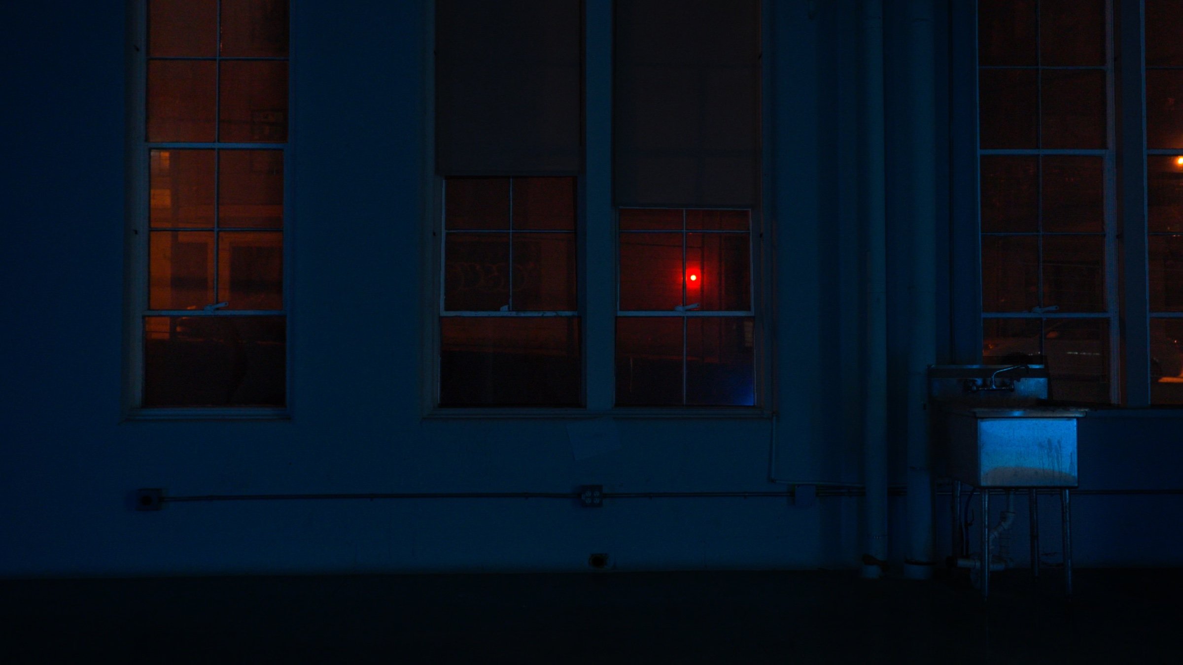 Tall windows at night, a single red light inside.